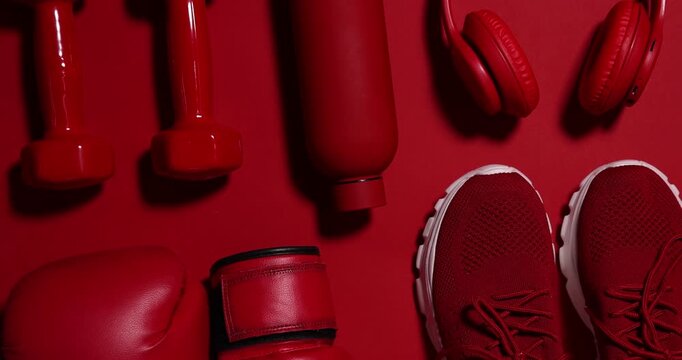 Sports equipment, water bottle, sneakers and headphones on red background, flat lay. Camera moving in
