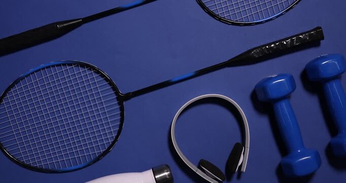 Sports equipment, water bottle and headphones on blue background, flat lay. Camera moving out