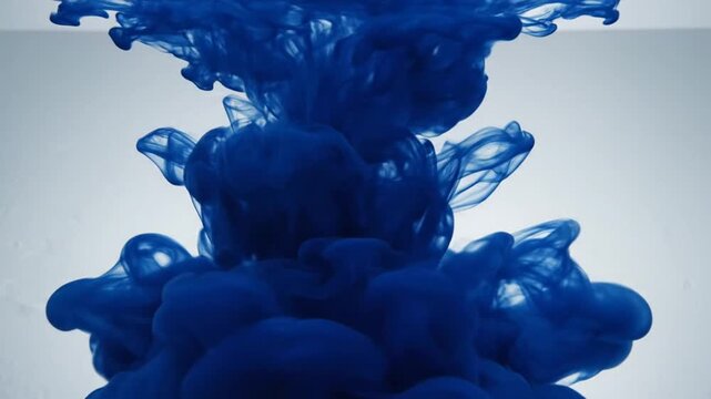 Dark blue ink diffusing in clear water creating abstract swirling patterns.