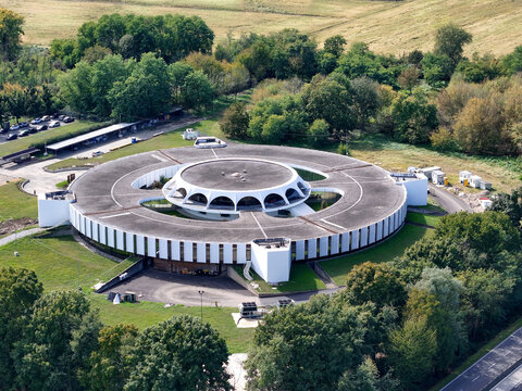 Aerial view of the Argotec SpacePark, a modern circular building surrounded by lush green trees and rolling fields in San Mauro Torinese, Piemonte, Italy.