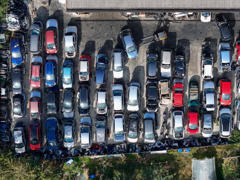 Aerial view of a car scrapyard with rows of abandoned and wrecked vehicles parked in an organized lot under bright sunlight Settimo Torinese, Piedmont, Italy.