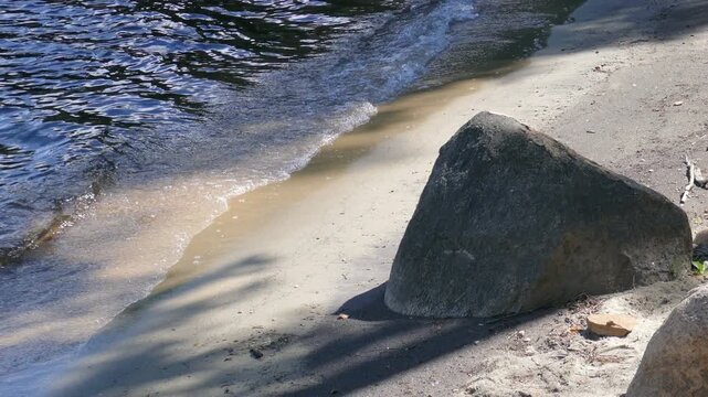 Small waves on a freshwater beach with a large rock. Lac Simon, a lake in Duhamel, Quebec, Canada.