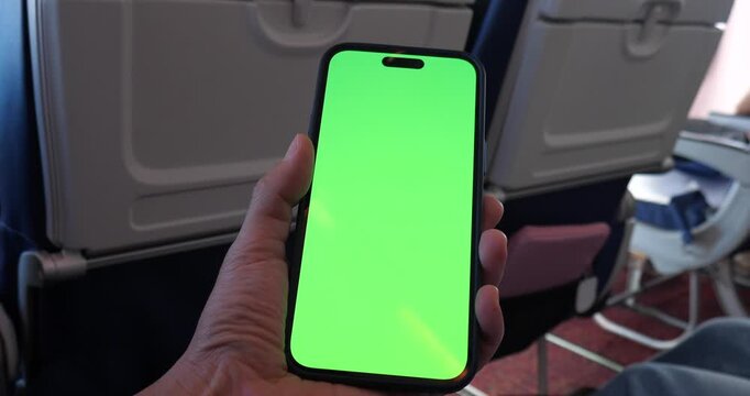 Cinematic close-up of a hand holding a smartphone with green screen chroma key on an airplane, flight background with window view