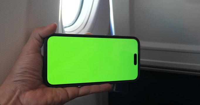 Cinematic close-up of a hand holding a smartphone with green screen chroma key on an airplane, flight background with window view