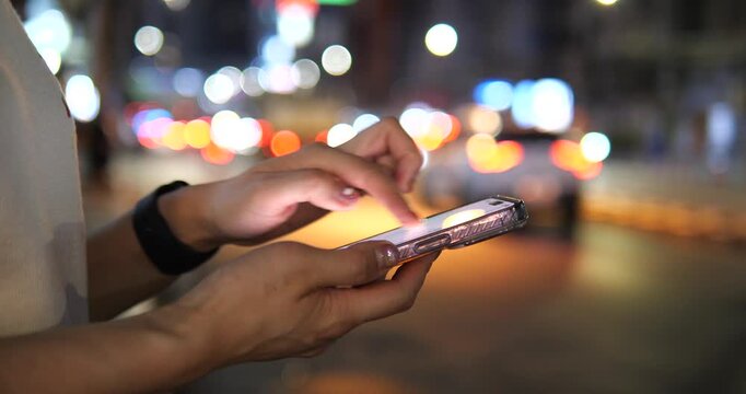 Cinematic close-up of hands using a smartphone on a city street at night, beautiful colorful bokeh background and urban lifestyle concept