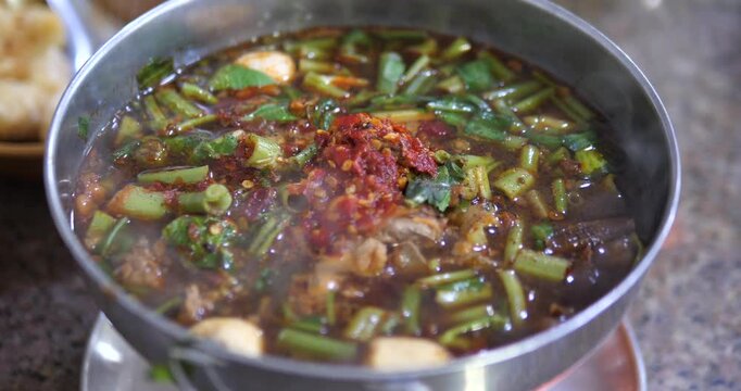 Cinematic close-up of Thai spicy braised beef soup (Gao Lao) in a hot pot, rich Tom Yum Nam Tok broth with chili paste and meatballs