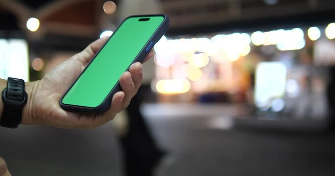 Cinematic close-up of a hand holding a smartphone with green screen chroma key, beautiful colorful city bokeh background at night