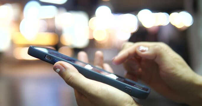 Cinematic close-up of hands using a smartphone on a city street at night, beautiful colorful bokeh background and urban lifestyle concept