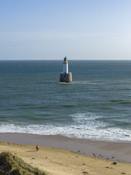 Aerial view of Rattray Head Lighthouse standing in the North Sea with people walking on the sandy beach under a clear blue sky Peterhead, Scotland, United Kingdom.