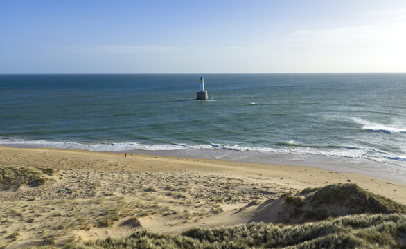 Aerial view of Rattray Head Lighthouse standing in the sea near a sandy beach with grassy dunes and people walking along the shore Peterhead, Scotland, United Kingdom.