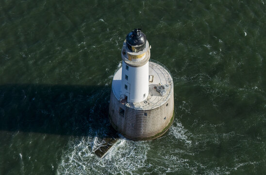 Aerial view of Rattray Head Lighthouse, a white tower standing in the dark green sea with gentle waves and white foam near Peterhead, Scotland, United Kingdom.