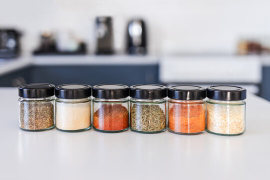 tidy spices and herbs in matching jars on kitchen countertop with soft kitchen bokeh background