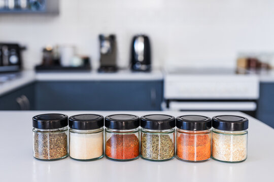 tidy spices and herbs in matching jars on kitchen countertop with soft kitchen bokeh background