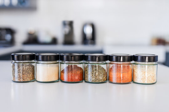 tidy spices and herbs in matching jars on kitchen countertop with soft kitchen bokeh background