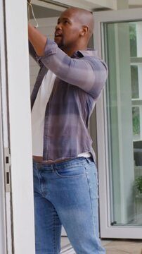 Vertical video: Spotting loose cord, man in plaid shirt reaching up at porch, fixing bell
