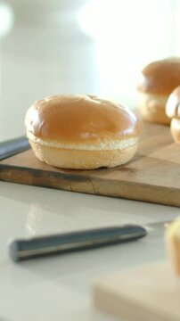 Vertical video: Racking focus, camera bringing knife and slice forward on counter, buns softening