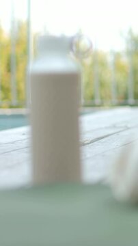 Vertical video: Camera racking focus blurring textured bottle on patio, showing towel and foliage