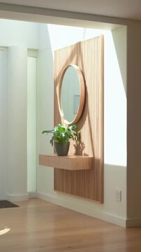 Vertical video: Sliding sunlight crossing slat wall, mirror and shelf at foyer, moving plant shadow