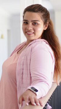 Vertical video: Looking back, woman at home in pink hoodie holding railing, watch on wrist, smiling