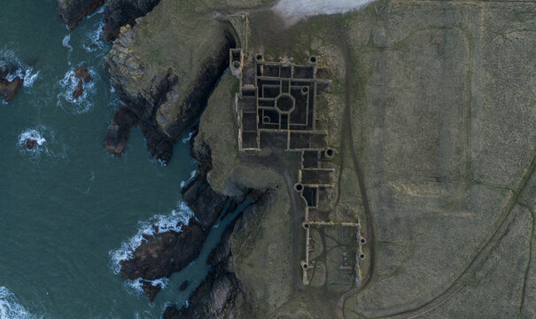 Aerial view of the historic ruins of Slains Castle perched on rugged cliffs overlooking the dark North Sea waves Cruden Bay, Scotland, United Kingdom.
