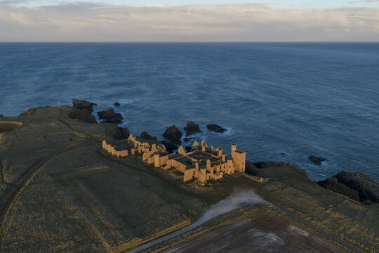 Aerial view of the historic Slains Castle ruins on the edge of steep cliffs overlooking the North Sea at golden hour in Cruden Bay, Scotland, United Kingdom.