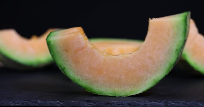 Melon lies on black slate, juicy slices of ripe melon with orange flesh and green peel on a dark stone surface with clear details and organic texture.