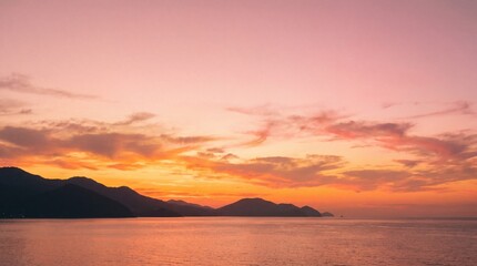 Obraz premium Warm sunset over calm sea with mountain range at horizon serene landscape