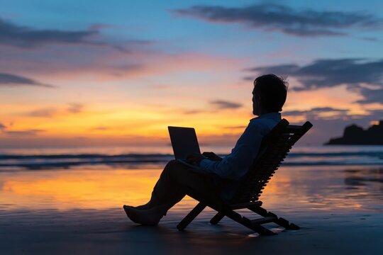 Man silhouetted working remotely on laptop at sunset beach