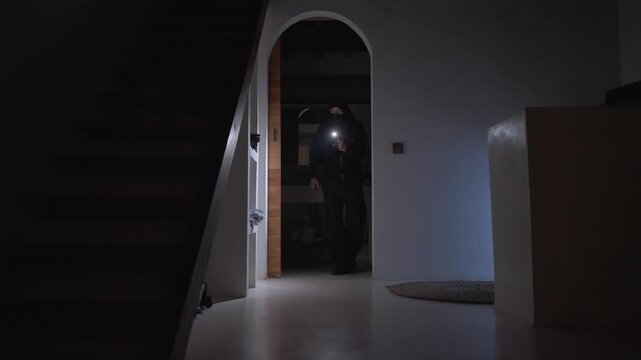 Burglar with flashlight robbing a house at night
