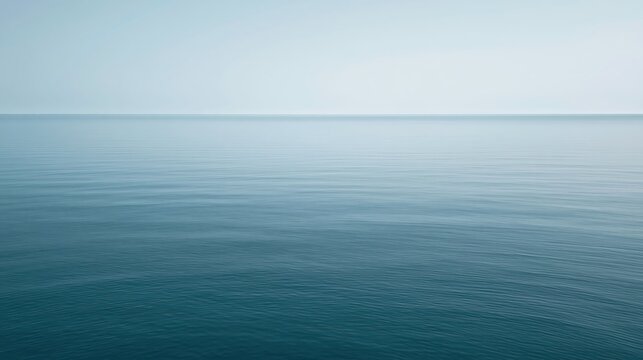 Calm ocean water stretches to the horizon under a clear, pale blue sky, creating a peaceful and minimalistic seascape.