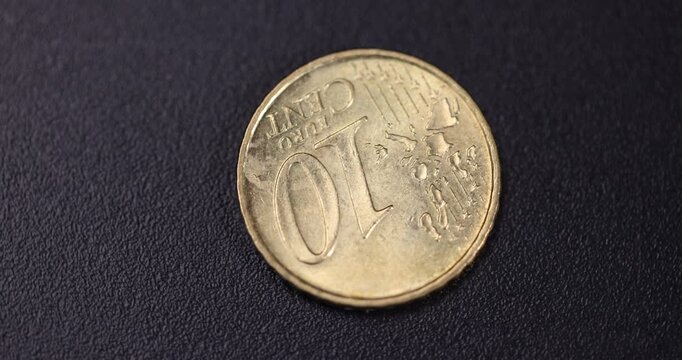 old 10-cent metal coins of the European Union, European money in the form of ten-cent coins with scratches lie on gray velvet, A coin is spinning in a circle on a black rotating platform