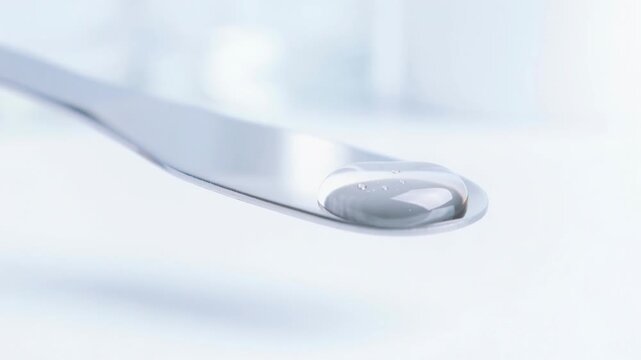 Close up slow motion video of clear medicine drop forming on shiny metal surface for health and pharmaceutical visuals