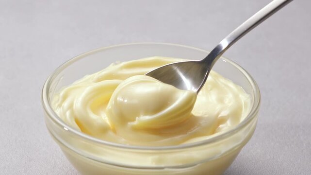 Close up of scooping creamy mayonnaise with a spoon from a glass bowl