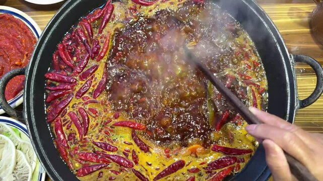 Detailed 120fps original footage of dried red peppers floating in a vigorously boiling spicy red oil hotpot.