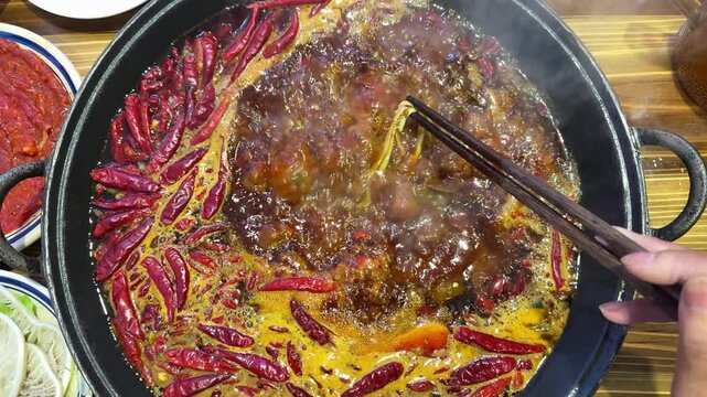 Extreme slow motion at 24fps capturing the artistic movement of red oil bubbles and steam in a spicy hotpot.