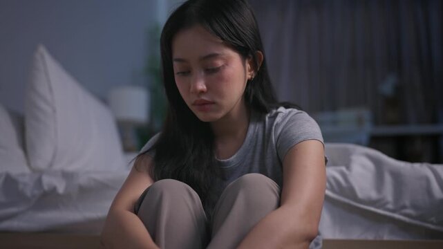 Depressed Asian young woman sitting alone on bedroom floor at night.
