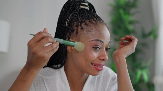 African American woman looking in the mirror while applying makeup.
