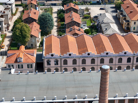 Aerial view of Villaggio Leumann featuring the historic factory with sawtooth roofs and a brick chimney among residential houses in Collegno, Piemonte, Italy.