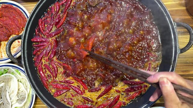 A horizontal shot of dipping meat into a spicy Sichuan hotpot with a speed ramp effect moving from normal to fast and back to normal.