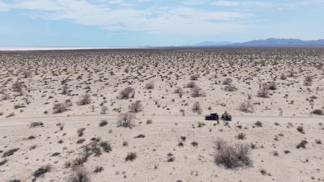 Aerial view shows an SUV pulling a teardrop camper trailer driving through the dry Baja desert near El Salar salt flats.