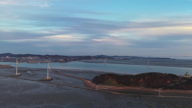 Panoramic drone shot of massive wind turbines standing on tidal flats along Tando Sea Road leading to Nue Island during golden hour in Ansan