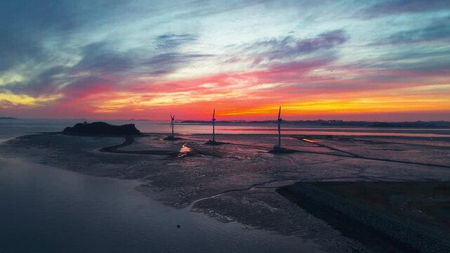 Drone shot of colorful sunset sky reflecting on tidal flats at Tando Port showing three wind turbines leading to Nue Island in Ansan South Korea during low tide