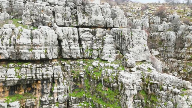 Natural rock cliff with cave-like openings and green vegetation in Qattin Azar, Baskinta, Lebanon, showing the rugged beauty and geological character of the area.