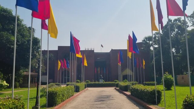 Entrance of the Shilpacharya Zainul Folk and Craft Museum in Sonargaon, with red, blue and yellow flags swaying in the wind on a clear sunny day at the cultural landmark