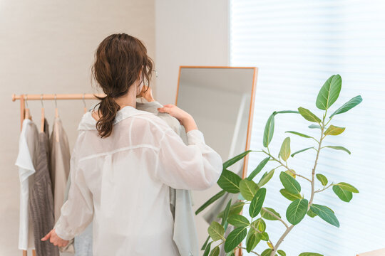 An Asian woman choosing clothes while looking in a full-length mirror (shopping, coordinating outfits, sale, shopping).