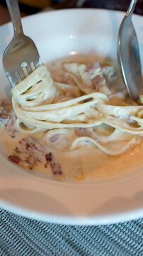 Close Up of Person Twirling Creamy Fettuccine Carbonara with Fork and Spoon