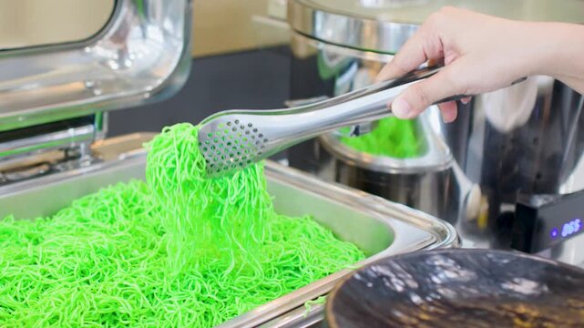Serving Green Jade Noodles from a Buffet Chafing Dish with Tongs