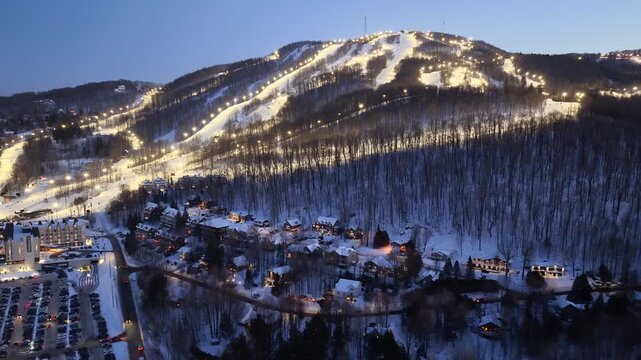Aerial drone view of illuminated Bromont ski resort slopes at dusk, Quebec, Canada in winter. g.
