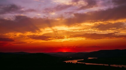 Fototapeta premium Vibrant golden hour sunset sky with deep orange and purple gradient over calm landscape
