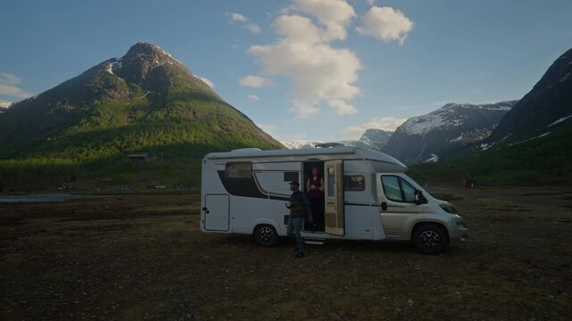 Camper parked off grid between mountains under a blue sky as a couple opens the door and steps outside to enjoy the view. Scenic van life moment with freedom and nature.